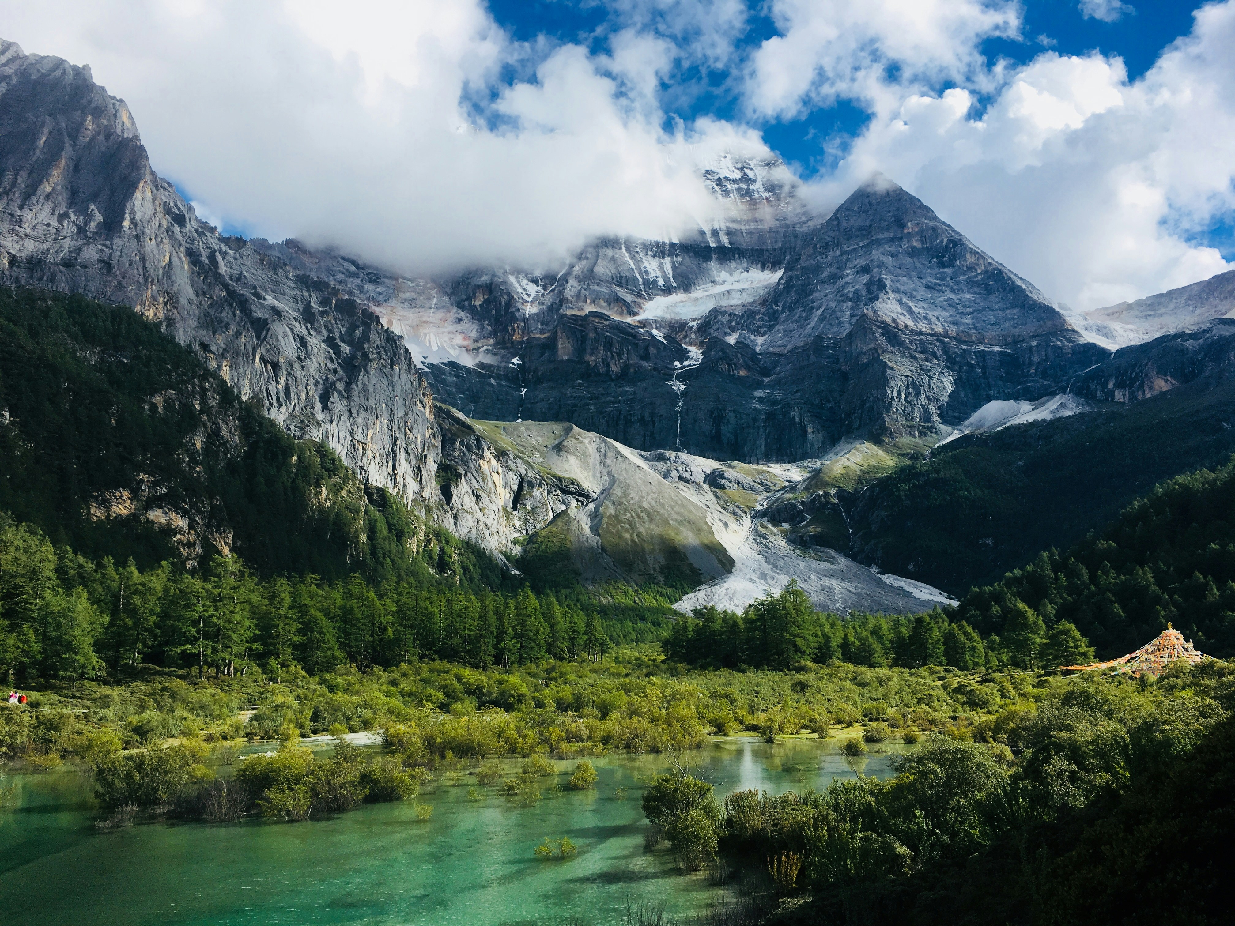 Turquoise glacial lake surrounded by dense forest and snow-capped peaks shrouded in cloud, Yading Nature Reserve, Daocheng, Sichuan, China